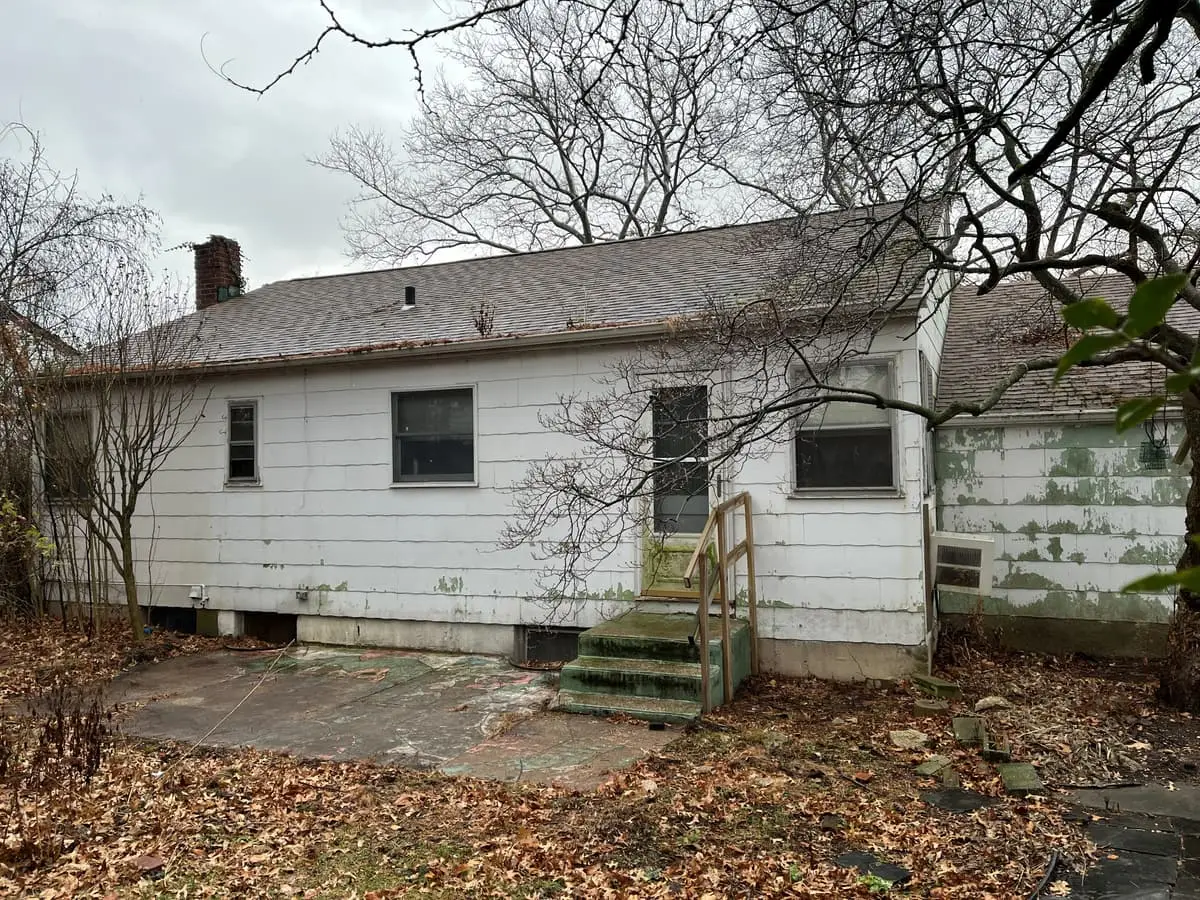 Selling a house with code violations in Plainview: back of a white house with mildewed siding and worn steps
