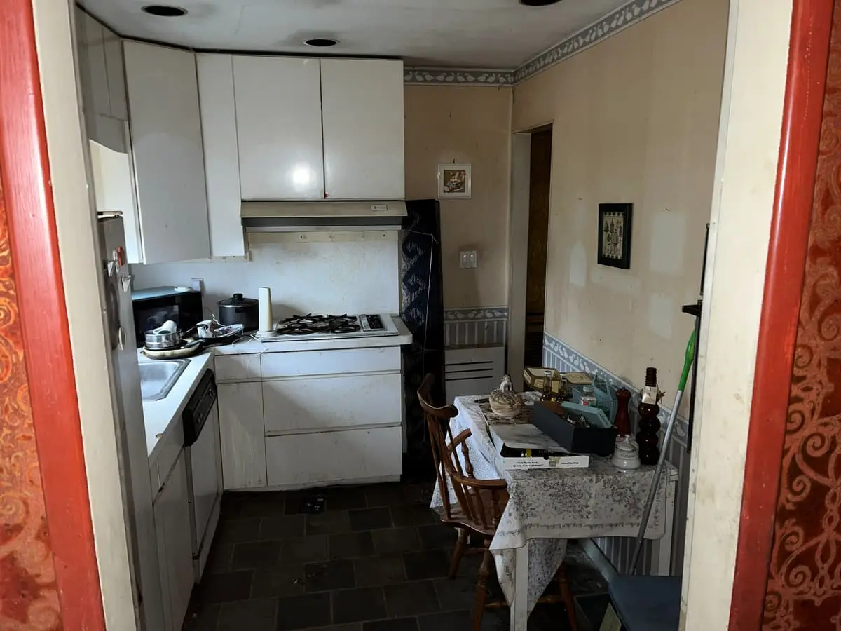 Selling a house with a reverse mortgage in Plainview: dated galley kitchen with white cabinets and patterned wallpaper