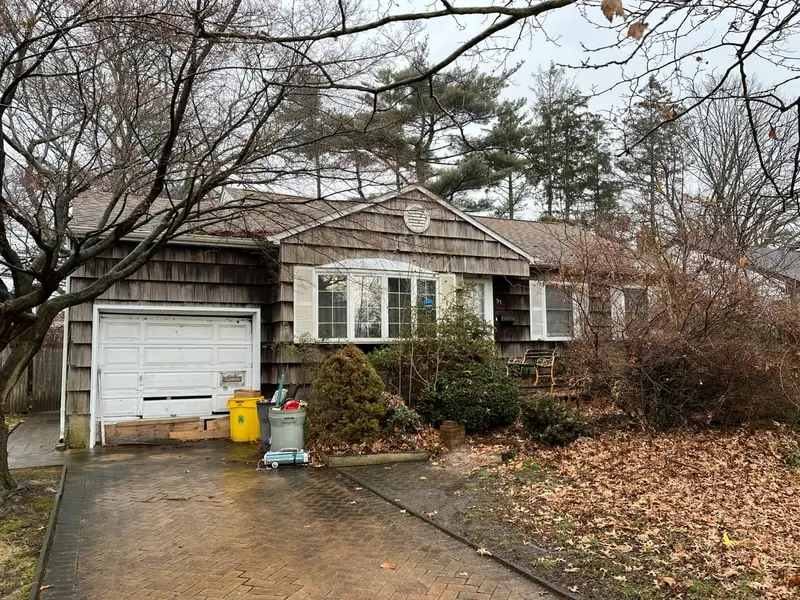 Shingled ranch with a garage behind overgrown shrubs, Plainview, NY